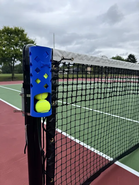 BallBar strapped to a tennis net post holding tennis balls courtside